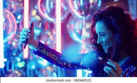 Closeup beautiful girl making selfie photo on mobile phone in nightclub. Portrait of brunette woman holding phone on neon lamps background. Pretty woman using smartphone at night club party - Powered by Shutterstock