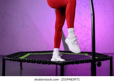 Close-up of beautiful muscular female legs in white sneakers on mobile mini trampoline. Energetic young fitness girl in red tracksuit. Jumping workout. High intensity interval cardio training - Powered by Shutterstock