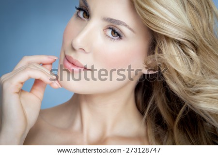 Closeup of beautiful natural blond woman with glowing skin over blue background.
