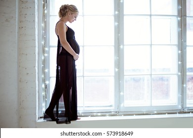 Closeup beautiful pregnant lady in elegant pose in black dress. Portrait of sexy fashion model girl in lingerie near window. Beauty sensual woman with attractive body indoors. Close-up female belly