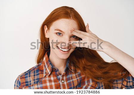 Close-up of beautiful redhead lady with blue eyes and pale skin, smiling at camera, standing over white background.