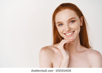 Close-up Of Beautiful Redhead Woman With Pale Skin, Standing Nude On White Background, Smiling With Perfect Teeth, Touching Clean No Makeup Face.