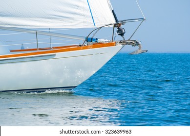 Closeup Of A Beautiful Sailboat Bow Cutting Through Beautiful Blue Water Under Full Sail On A Cloudless Sunny Morning.