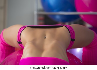 Closeup Of Beautiful Sexual Belly Of Fitness Woman With Musculat Body Lying In Erotic Pose On Big Pink Ball In Sport Hall Training Indoor, Horizontal Picture