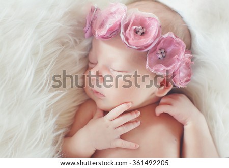Close-up beautiful sleeping baby girl. Newborn baby girl, asleep on a blanket. A portrait of a beautiful, seven day old, newborn baby girl wearing a large, fabric rose headband. Closeup photo