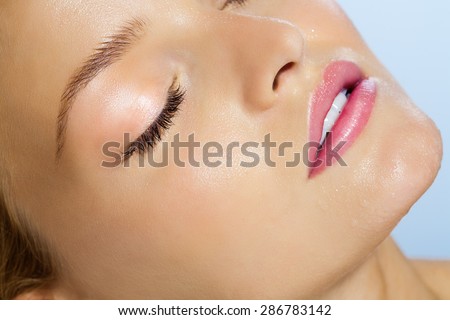 Closeup of beautiful smooth young dewy skin with water drops over sky blue background. Serene woman with eyes closed in summer sun.
