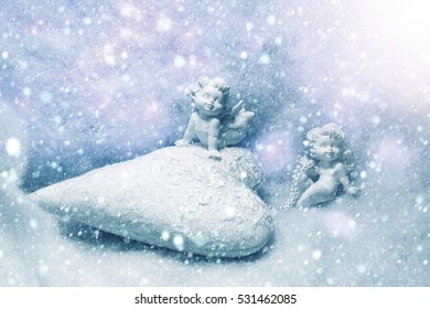 Closeup of beautiful soulful figurine composition of cupid angels for valentine day or christmas with small pillow in shape of heart lying on white wadding decorating snow with purple light sparks - Powered by Shutterstock