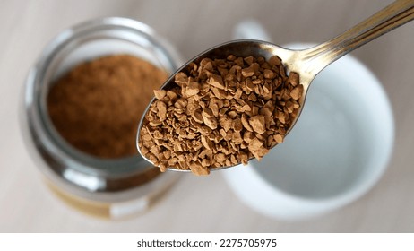 Close-up of a beautiful spoon filled with freeze-dried instant coffee above the coffee jar and an empty cup on the table