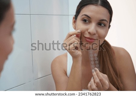 Close-up of beautiful woman applying acne treatment anti-pickel patch on a pimple in bathroom