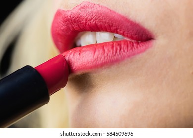 Close-up of beautiful woman applying red lipstick on lips against black background