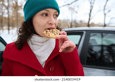 Close-up. Beautiful Woman, Female Driver Eating Take Out Food, Delicious Baked Cookies, Standing Near Her Automobile In The Snowy Forest During Her Trip By Car. Wonderful Winter