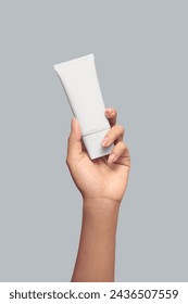Closeup of beautiful woman hand holding white cream tube. Isolated on grey background