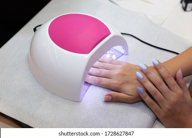Close-up Beautiful Woman Hands And Lamp For Nails On Table. Nail Gel Salon. UV Lamp. Process Of Drying Gel On Nails. Beauty And Self Care. Modern Technology In Nail Salon. Nail Care After Quarantine