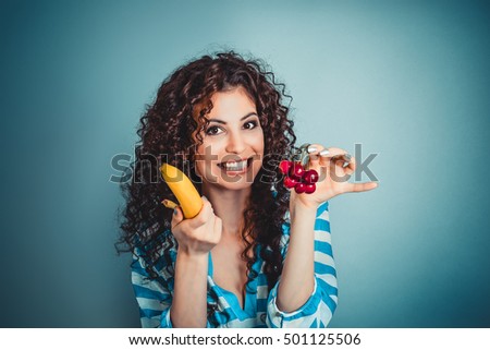 Closeup beautiful woman showing giving choosing to eat banana or cherry fruits isolated blue background wall. Healthy lifestyle concept