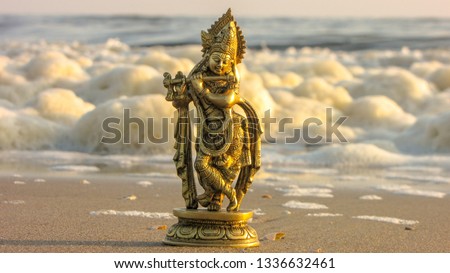 Closeup of a beautiful yellowish metal statue of Lord Krishna put on the sand beach