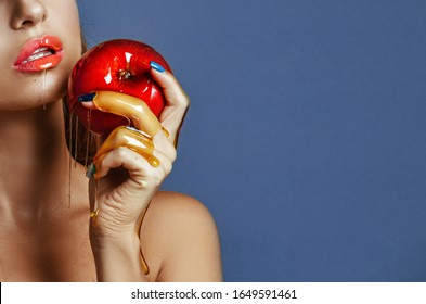 Close-up of beautiful young girl with a smooth tanned skin holding a shiny apple. Girl biting fresh red honey apple over blue background. Healthy eating. Fruits and vegetables.