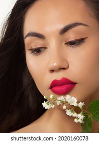 Close-up beauty of female face withevening make-up. Black arrows on the eyes and extremely long eyelashes, on full pink lips matte scarlet lip color. Well-groomed skin. white flowers