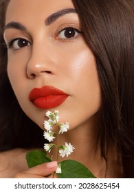 Close-up beauty of female face withevening make-up. Black arrows on the eyes and extremely long eyelashes, on full red lips matte scarlet lip color. Well-groomed skin. white flowers