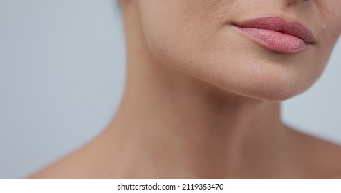 Close-up beauty portrait of young woman softly touches her chin with a back of her hand, gently lays fingers on the jowl and smiles and looking at the camera. Skin care cosmetology.