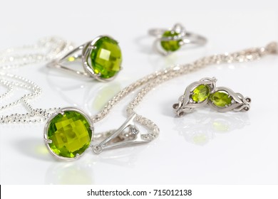 Close-up beauty silver earrings and pendant with peridot on background  chain and rings on white acrylic desk.