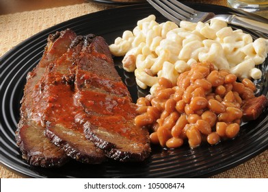 Closeup of beef brisket smothered in barbecue sauce with boston baked beans and macaroni salad