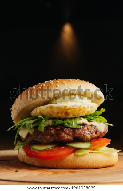 Close-up of\
beef burger with poached egg. Hamburger - bun, grilled meat\
burger,arugula salad,\
tomato and fried\
egg.