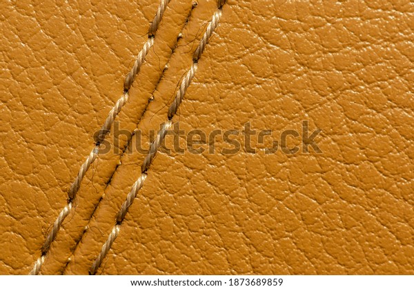 Close-up of beige\
orange faux leather stitching in the car interior. Background for\
interior trim comfort