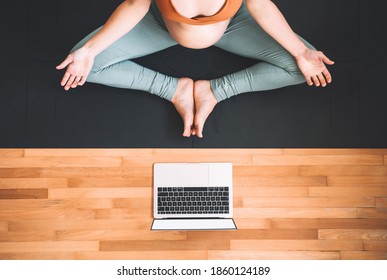 Closeup Belly Of Pregnant Woman Practicing Yoga Online At Home With Laptop. Expectant Mother Doing Prenatal Yoga Class Or Meditating During Pregnancy Indoors. Healthcare Of Mother And Unborn Baby.