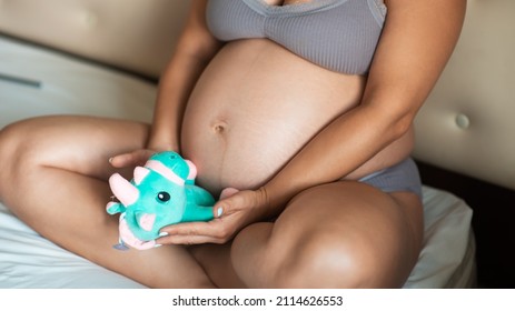 Close-up of the belly of a pregnant woman with a soft toy. The concept of pregnancy, parenthood, preparation and waiting. pregnant belly, natural skin. stretching marks on abdominal skin