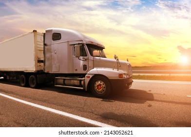 Close-up Of A Big Grey American Truck With A White Trailer On A Countryside Road Against A Blue Sky With A Sunset