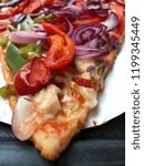 Closeup of a big thin slice of vegetable pizza served on a white paper plate.