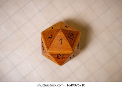 Close-up, big wooden 20 sided dice showing a bad roll of a natural 1. The die is on a grid mat map used for roleplaying party board games which explore dungeons on nerdy quests.