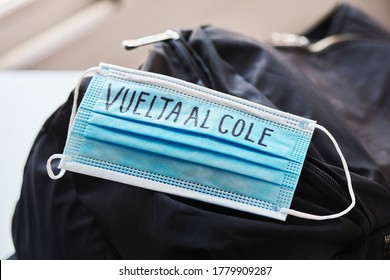 Closeup Of A Black Bookbag And A Blue Surgical Mask With The Text Back To School Written In Spanish, Depicting The Need To Prevent The Infection At School In The Covid-19 Pandemic Situation