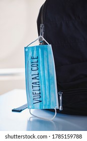 Closeup Of A Black Bookbag And A Blue Surgical Mask With The Text Back To School Written In Spanish, Depicting The Need To Prevent The Infection At School In The Covid-19 Pandemic Situation