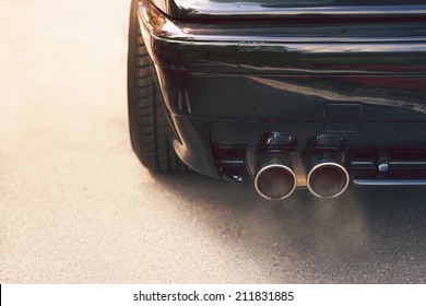 Close-up of black car dual exhaust pipe with smoke