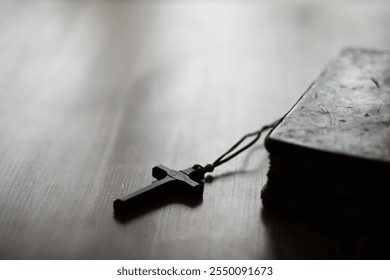 Close-up of a Black Cross Pendant on a Wooden Surface with an Old Leather-bound Book in Soft Focus Background - Powered by Shutterstock