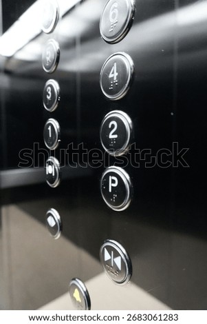 Close-up of black elevator control panel with illuminated metallic buttons showing floor numbers and parking level, modern lift interior design with reflective surface and chrome details.