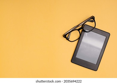 Closeup black eyeglasses and ebook reader on yellow background. Flatlay