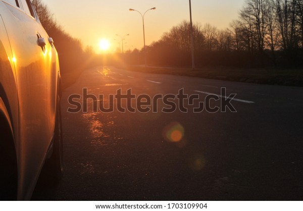 Close-up of a black family car on an asphalt road\
with trees and a bright\
sunset