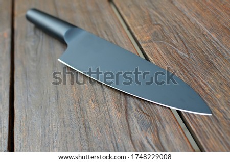 Close-up of a black kitchen knife on a wooden table. Matte finishing, flat lying, perspective view, focus on foreground