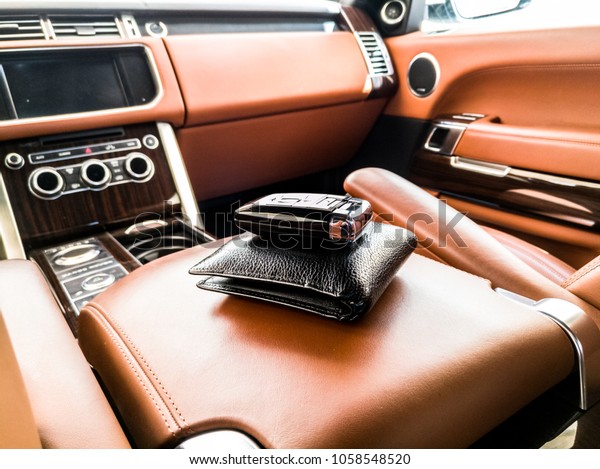 closeup of a black leather wallet and a car\
key kept it inside an exotic vehicle with brown interior of the car\
in the background