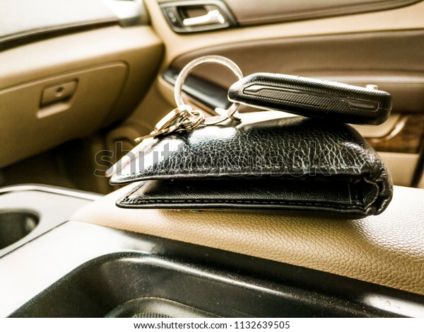 closeup of a black leather\
wallet and a car key kept on it inside an exotic vehicle in grey\
interior