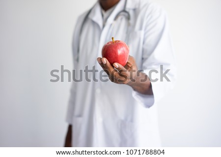 Closeup of black male doctor holding and offering red apple. Healthy nutrition concept. Isolated front view on white background.