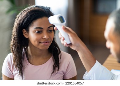 Closeup Of Black Man Doctor Checking Patient Pretty African American Woman Body Temperature, Using Electronic Thermometer, Young Lady Having Checkup Before Vaccination Against Coronavirus