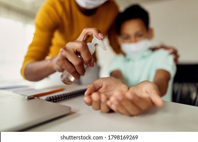 Close-up of black mother using hand sanitizer and cleaning son's hands at home during coronavirus epidemic.  - Powered by Shutterstock