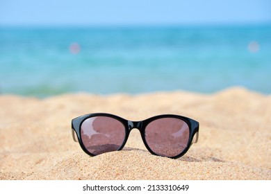 Closeup of black protective sunglasses on sandy beach at tropical seaside on warm sunny day. Summer vacation concept. - Powered by Shutterstock