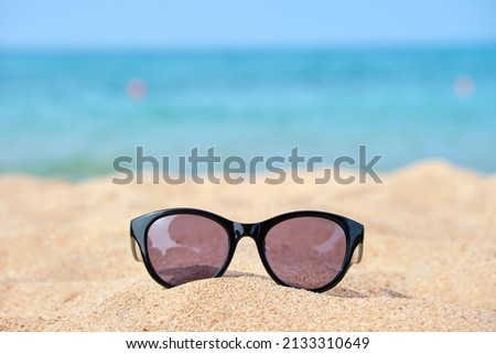 Closeup of black protective sunglasses on sandy beach at tropical seaside on warm sunny day. Summer vacation concept.