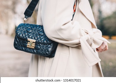 Closeup Of A Black Quilted Handbag Hanging From The Shoulder Of A Young Woman Wearing A White Coat.