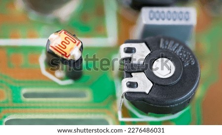 Closeup of black resistor trimmer and photoresistor with sensitive surface in a green PCB. Small electrical components on blurred printed circuit board detail. Optoelectronics in electronics industry.