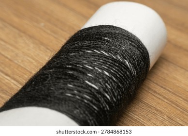 Closeup black sewing thread spool on wooden background showing textile material for tailoring craft and stitching work